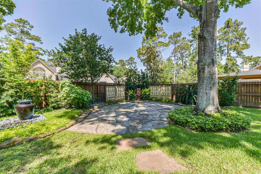 Charming backyard with a spacious stone patio, mature trees, and lush landscaping, offering a serene outdoor retreat.