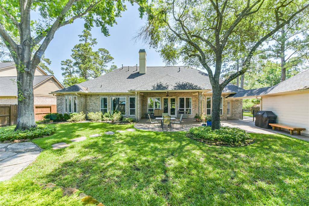 This photo showcases a charming backyard with a spacious patio, mature trees, and well-maintained lawn. The brick exterior of the house offers a classic look, complemented by large windows and a cozy outdoor seating area, perfect for relaxation and entertaining.