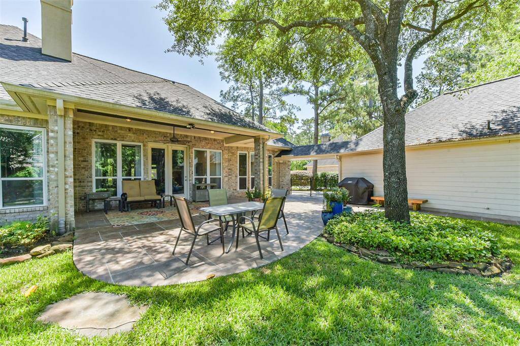 Charming backyard with a spacious patio ideal for entertaining. Features include a covered seating area, outdoor dining set, grill space, and lush greenery under a mature tree. Perfect for enjoying sunny days and outdoor gatherings.