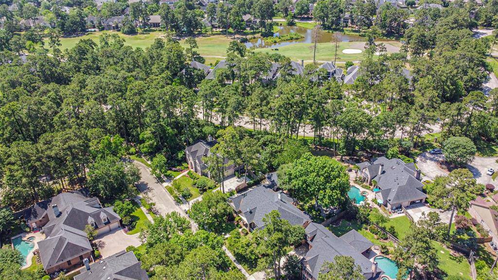 This aerial photo showcases a lush, wooded neighborhood with spacious homes, some featuring pools. The area is adjacent to a golf course, offering scenic views and a serene environment. Ideal for buyers seeking privacy and natural beauty.