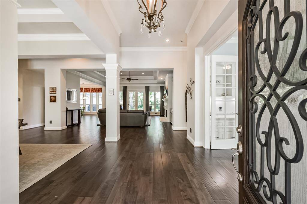 This elegant entryway features rich hardwood floors, high ceilings, and an ornate chandelier. It opens to a spacious living area with large windows offering plenty of natural light. The design combines modern and classic elements with a welcoming ambiance.