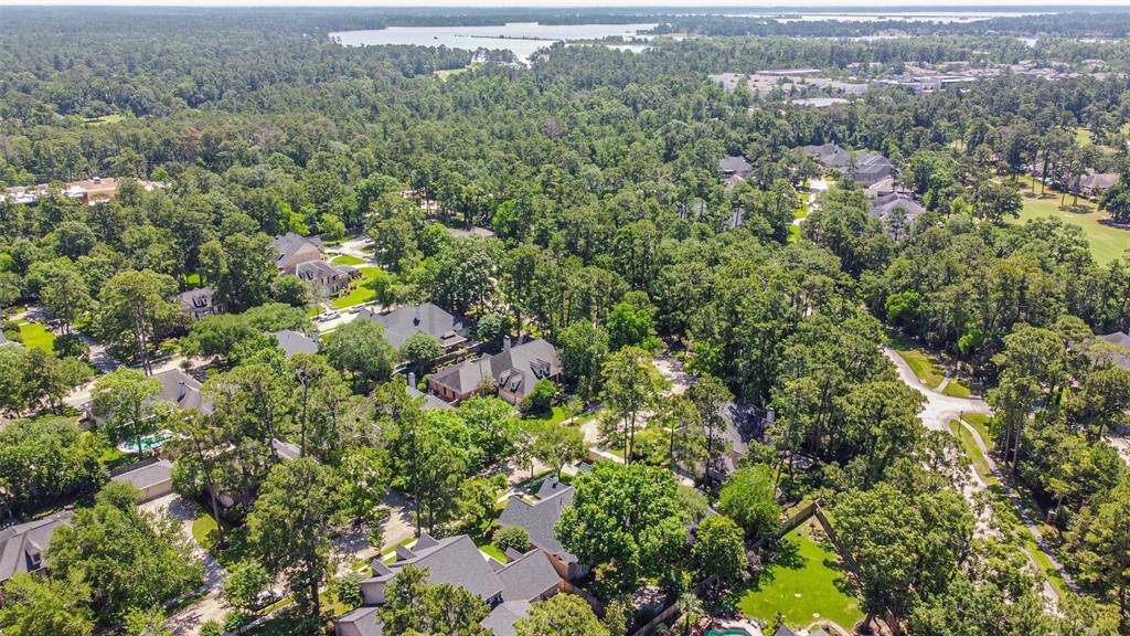 This aerial photo showcases a serene residential neighborhood surrounded by lush greenery and mature trees. The homes are spacious and well-spaced, providing privacy and a tranquil environment. The area features winding streets and is close to a large body of water, offering scenic views and a peaceful atmosphere. Ideal for buyers seeking a blend of nature and community living.