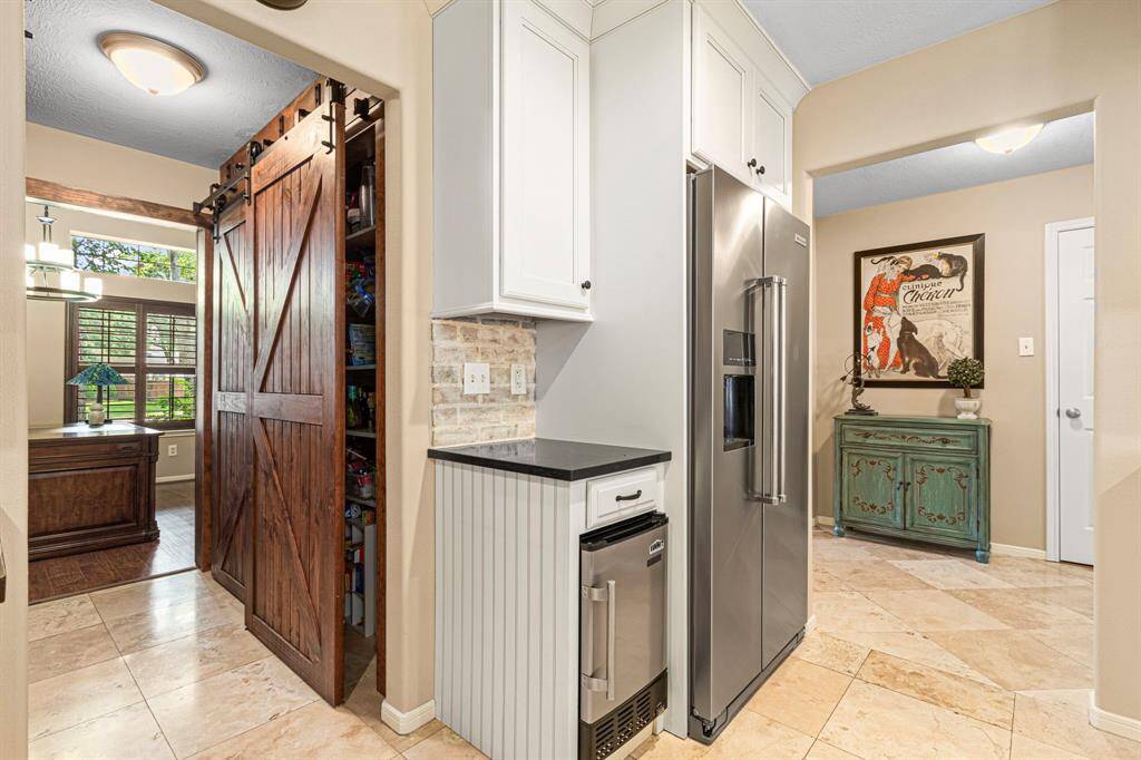From the kitchen, a view toward the front office showcases a sleek, SS refrigerator and a built-in under-the-counter ice maker--(both convey with the home!)  stylishly integrated into the cabinetry and positioned for easy access while entertaining or prepping meals.