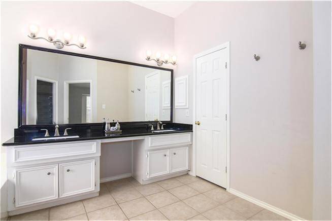 This primary bathroom features a spacious double vanity with a sleek black countertop and ample cabinet storage. Large mirror, elegant lighting fixtures, and neutral tile flooring, creating a clean and bright atmosphere.