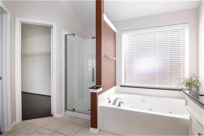 Primary bathroom features a spacious jetted tub, a separate glass-enclosed shower, and plenty of natural light from a large window with blinds.