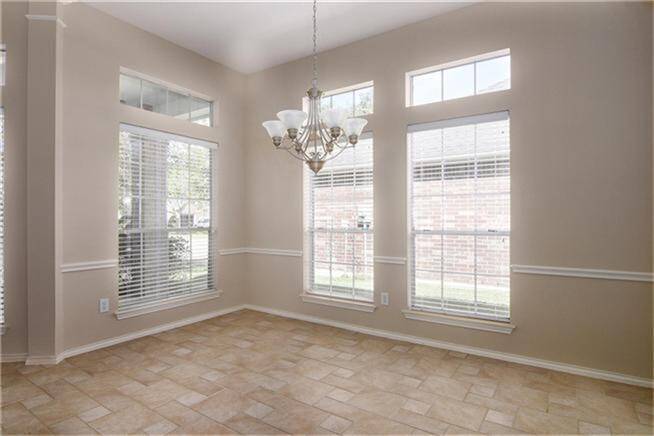 Bright dining area featuring large windows with blinds, allowing natural light. The space includes a chandelier and neutral tiled flooring, creating a warm and inviting atmosphere.