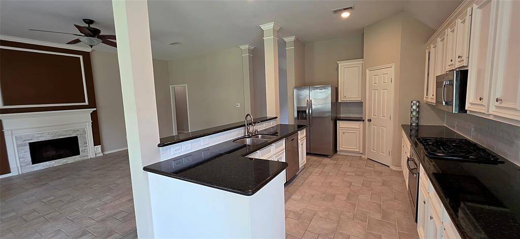 This spacious, open-concept kitchen and living area with tiled floors and high ceilings. The kitchen features modern stainless-steel appliances including fridge/freezer, and granite countertops. The living area includes a cozy fireplace and ample natural light, creating a welcoming atmosphere.