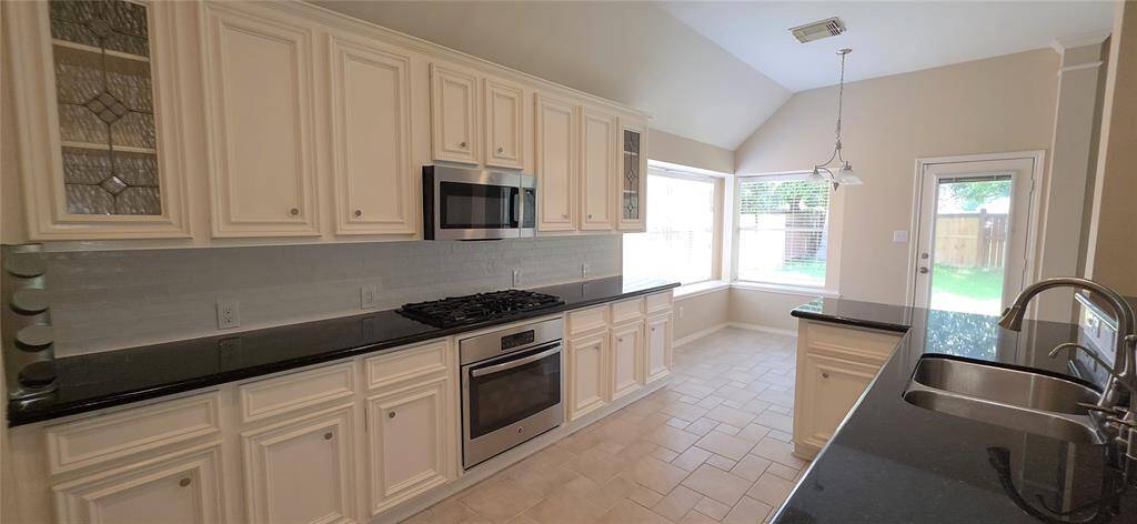 This kitchen features modern white cabinetry with decorative glass inserts, a sleek black granite countertop, and stainless steel appliances including a built-in oven and microwave.