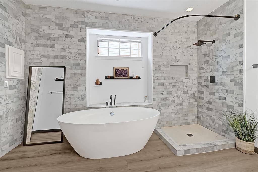 The primary bathroom boasts a sleek freestanding tub, open walk-in shower, and stunning floor-to-ceiling tilework for a luxurious spa-like feel.