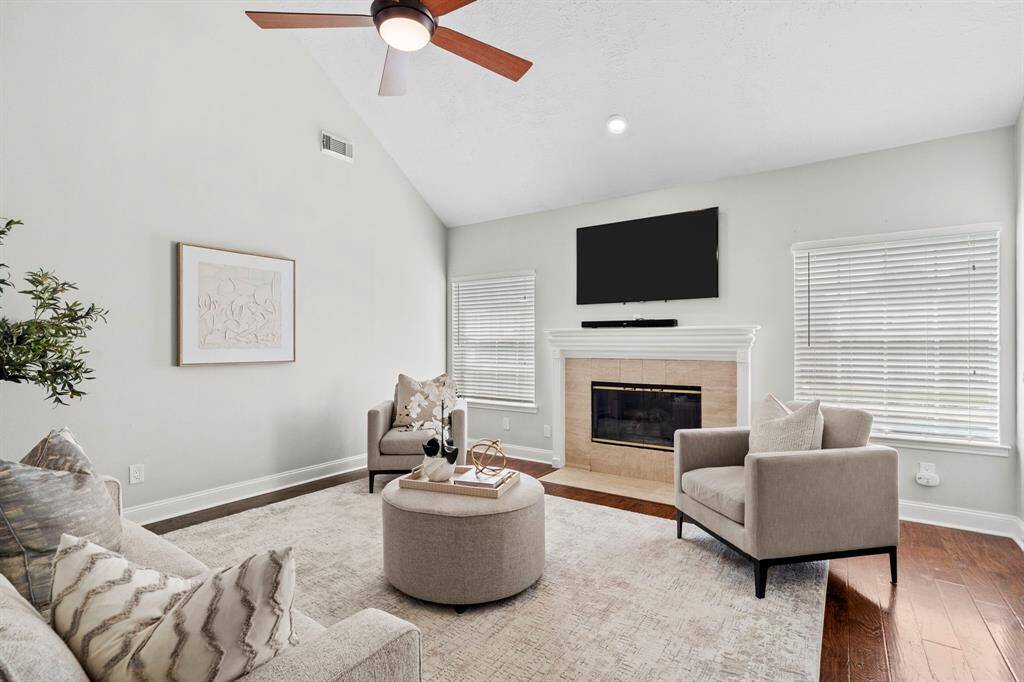 The family room features soaring ceilings, rich laminate flooring, and a cozy gas fireplace framed by windows that invite soft natural light into the space.
