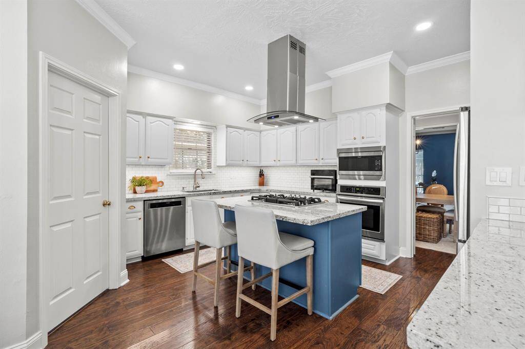 The updated kitchen features granite countertops, white cabinetry, stainless steel appliances, and a large island with a gas cooktop and seating for two.