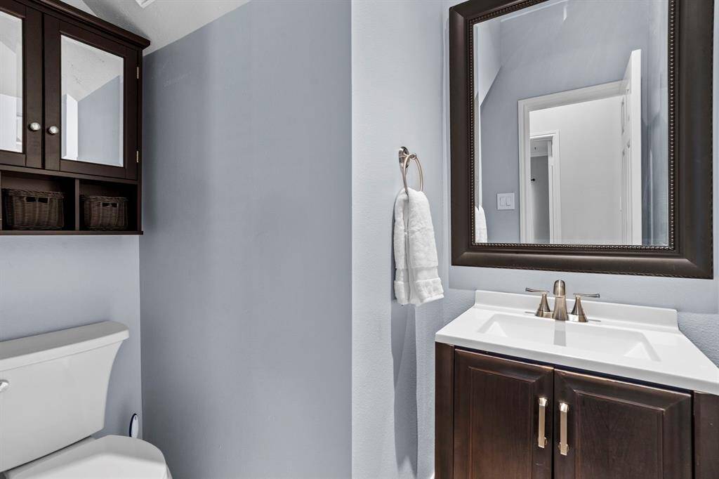 This stylish half bathroom features a sleek dark wood vanity with a modern rectangular sink, a framed mirror with beaded detailing, and a matching wall cabinet that offers additional storage and organization.