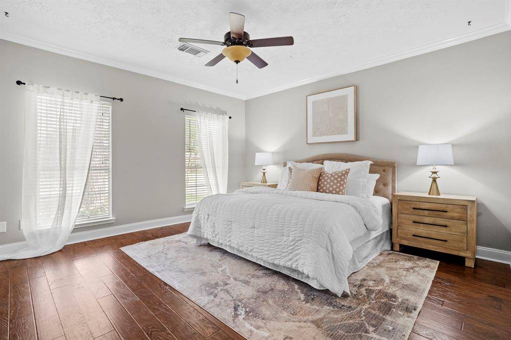 The spacious primary bedroom offers a serene retreat with warm wood-look laminate flooring, soft neutral tones, and abundant natural light streaming through dual front-facing windows.