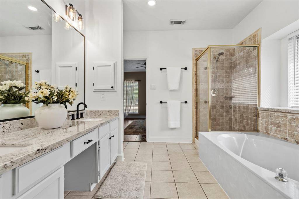 The en suite bathroom features a granite-topped dual vanity, a framed mirror with updated lighting, and a walk-in shower with natural stone tile for a spa-like experience.
