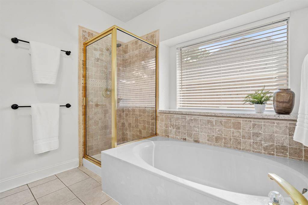 Unwind in the oversized soaking tub framed by travertine tile and a large picture window, set beside a separate walk-in shower for added convenience and comfort.