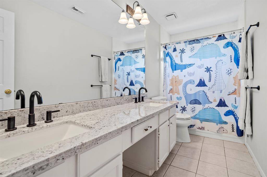 The upstairs guest bathroom features a dual-sink vanity with granite countertops, updated matte black fixtures, and a tub/shower combo—perfect for busy mornings or evening wind-downs.