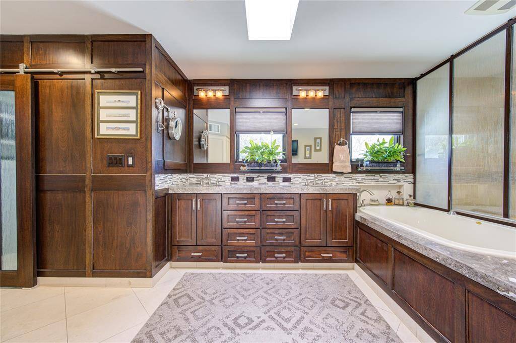 Handsomely outfitted primary bathroom is bathed in natural light from perfectly positioned skylight, has dual vanities, jetted soaking tub and stylish shower.
