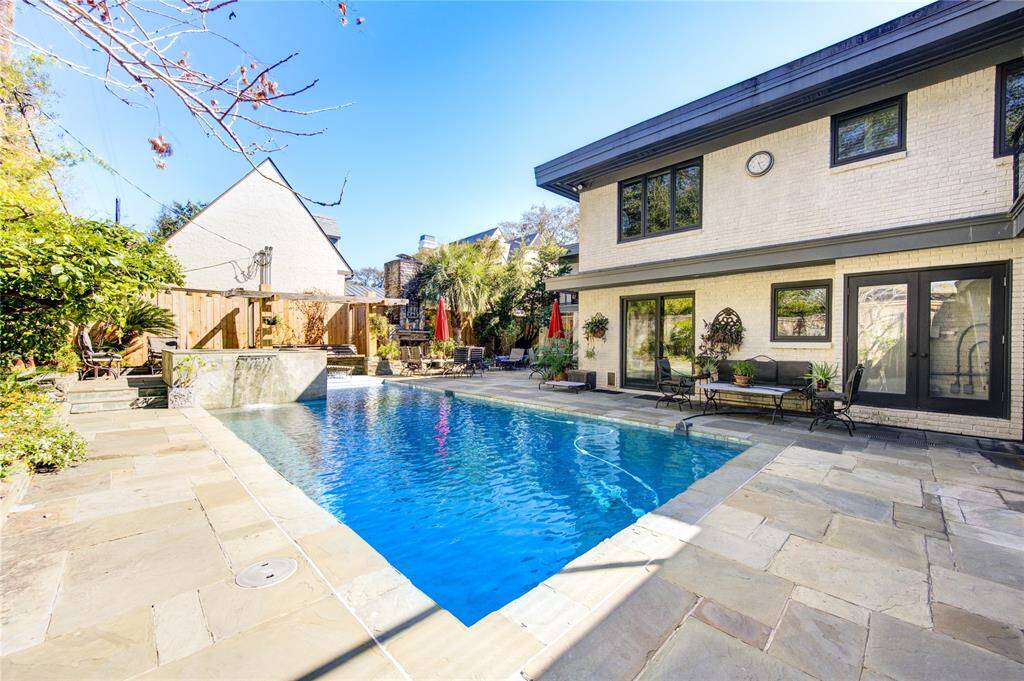 Showcasing the spacious backyard featuring a modern, rectangular swimming pool surrounded by a stone patio. The area includes outdoor seating areas, lush greenery, and a charming pergola, offering a perfect setting for relaxation and entertainment.