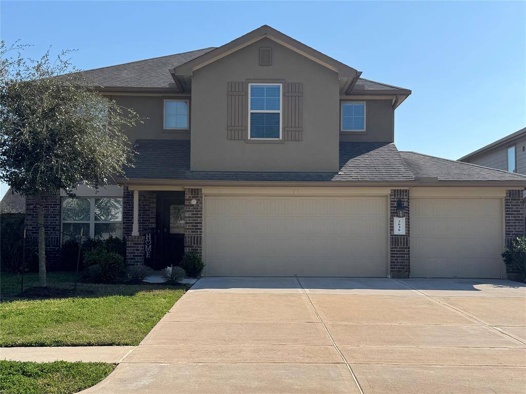 Two-story, contemporary home features a neutral-toned exterior with brick and siding accents. It has a large three-car garage and ample driveway space. The house is situated in a suburban neighborhood.