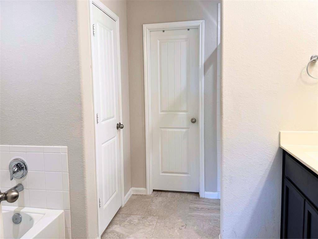 Primary bathroom with neutral walls and tile flooring. It features a bathtub with a tiled surround, a vanity with a light countertop, and two paneled doors, offering a clean and modern appearance.