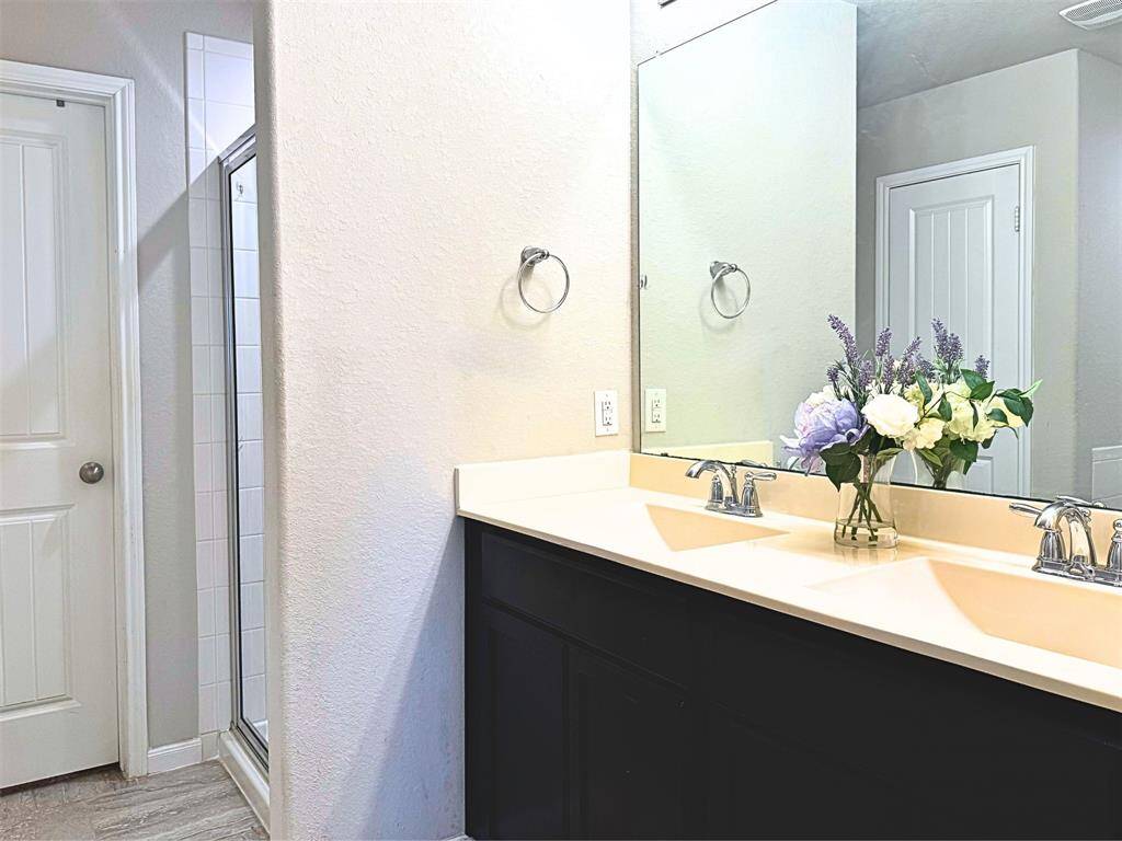 Primary bathroom features a double vanity with dark cabinets and a large mirror. It also includes a glass-enclosed shower and modern light fixtures