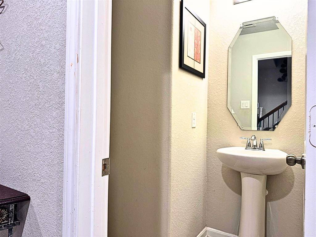 Half bathroom downstairs features a pedestal sink and an octagonal mirror. The space is neutral-toned and has a textured wall finish.