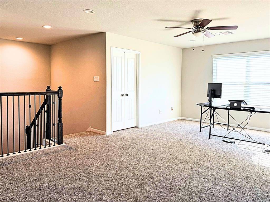 Game room with ceiling fan, ample natural light from a large window, and a stylish black stairway with a railing