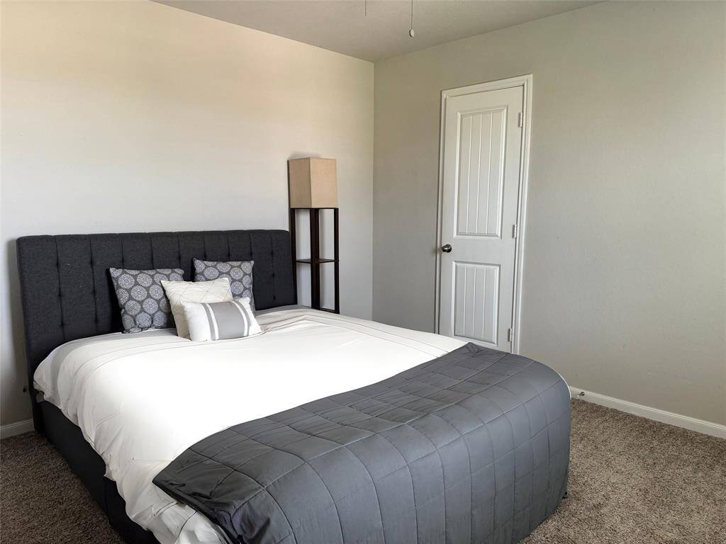 Cozy bedroom features soft carpet flooring, ample natural light from a window with blinds, and neutral walls that create a calm atmosphere, perfect for relaxation.