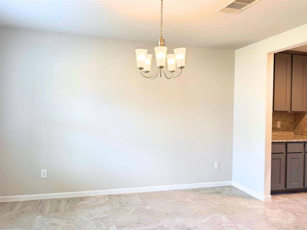 Dining area with tiled floors and a modern light fixture. The walls are neutral, and there's a partial view of the kitchen, cabinetry, and a tiled backsplash.