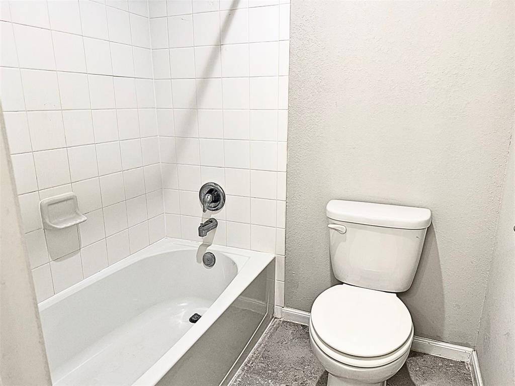 Bathroom features a bathtub with a tiled shower surround and a standard toilet. The walls are painted in neutral tones, creating a clean and simple look.