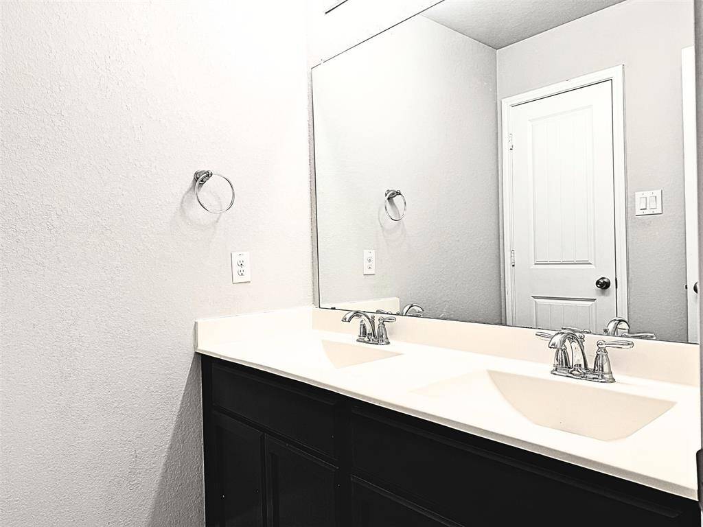Modern bathroom features a double vanity, sleek dark cabinets, a large mirror, and a neutral color palette. The space also includes chrome fixtures and a door leading to the game room.