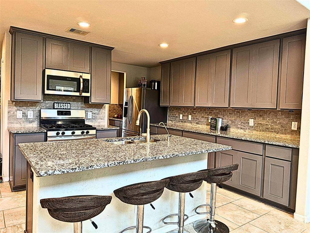 Modern kitchen with granite countertops, stainless steel appliances, and ample cabinetry. Features a large island with seating and stylish tile backsplash. Perfect for cooking and entertaining.