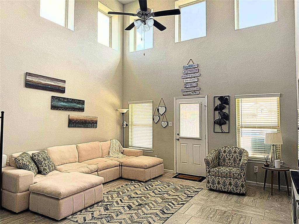 Bright and spacious living room with high ceilings, featuring large windows, a ceiling fan, and a neutral color palette creates an inviting space for relaxation.