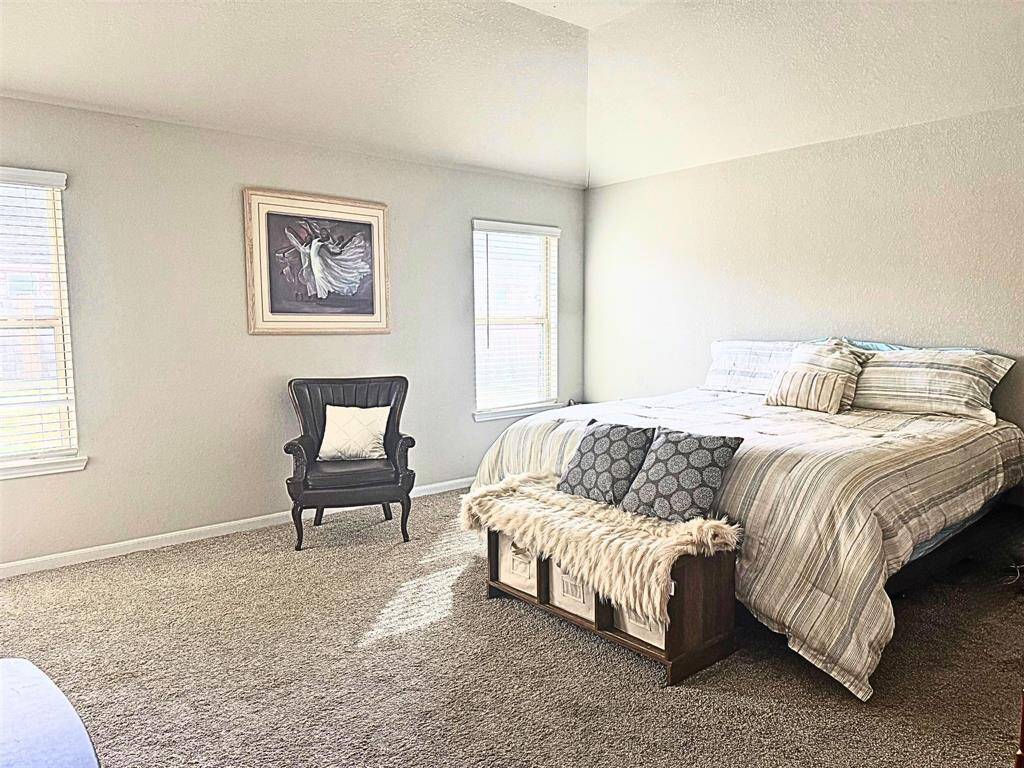 Spacious, well-lit primary bedroom with high ceilings and neutral tones creates a serene atmosphere. Soft carpeting and large windows invite natural light.
