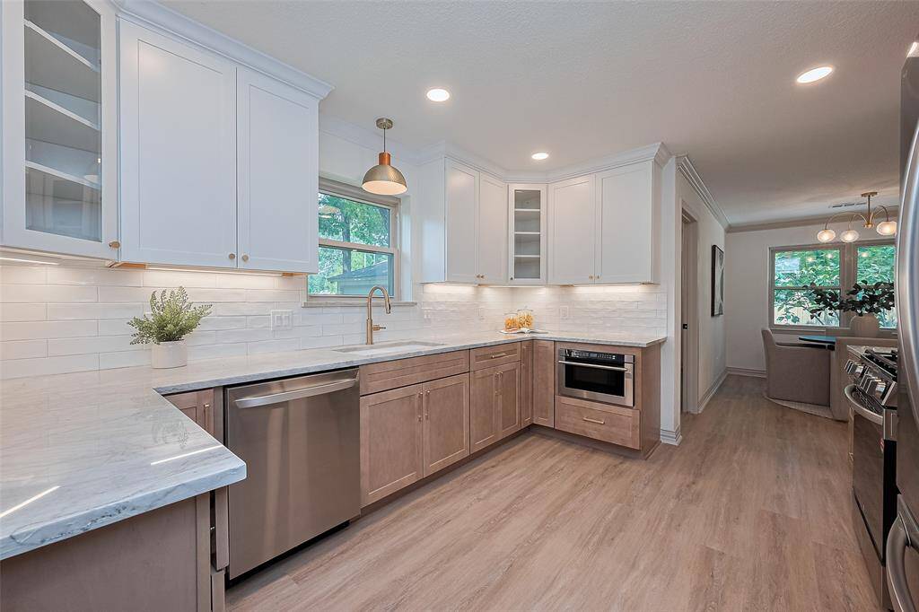 This modern kitchen features sleek white cabinetry, amazing quartzite counters, stainless steel appliances, top notch dishwasher and counter microwave drawer that soft closes, and light wood flooring. Abundant natural light complements the elegant pendant lighting, creating a bright and inviting space.