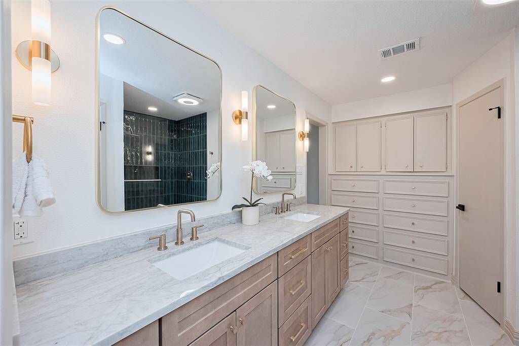 Beautiful Primary Bathroom with built in storage cabinets with drawers, pretty tiled floors, custom cabinetry, quartz countertops, double sinks, large mirrors, recessed and wall lighting with dimmer switches.