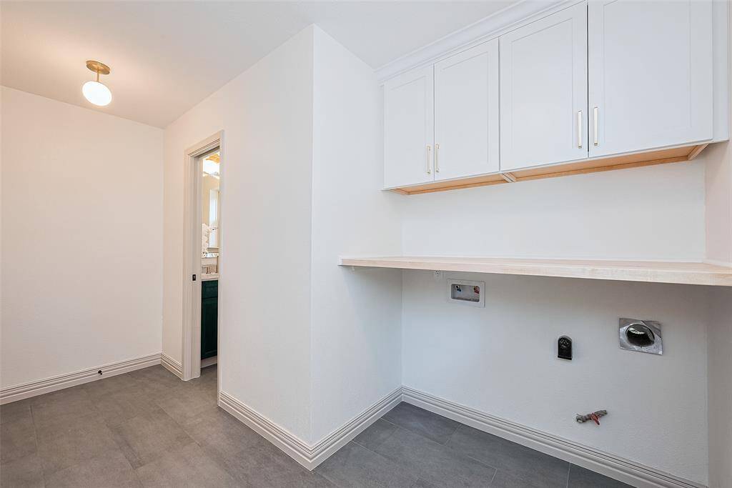 This photo shows a bright, laundry room with overhead custom cabinets, functional clothes folding shelf, tile flooring, washer and gas or electric dryer connections. Makes a great mud room with a new door for back yard and garage access.