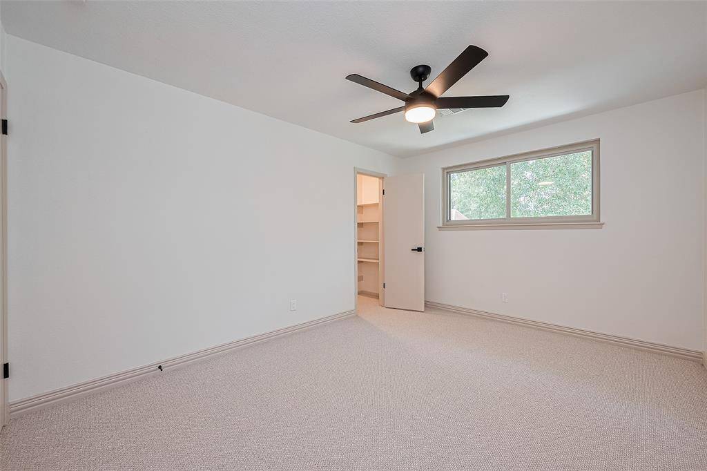 Upstairs 2nd of 3 spacious bedroom featuring neutral walls and soft carpet, a modern ceiling fan, a large window, and a walk-in closet with built-in shelving. Can be a bedroom, playroom, craft room, another office, workout area, or anything of your choosing.