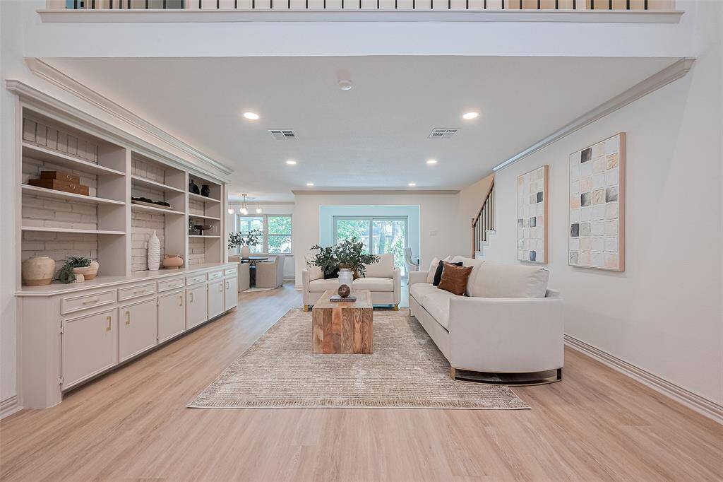 This spacious living room features a cozy brick fireplace, built-in shelving, and modern lighting. Brand new modern colors and high-end luxury vinyl plank floors create an inviting atmosphere for family or entertaining.