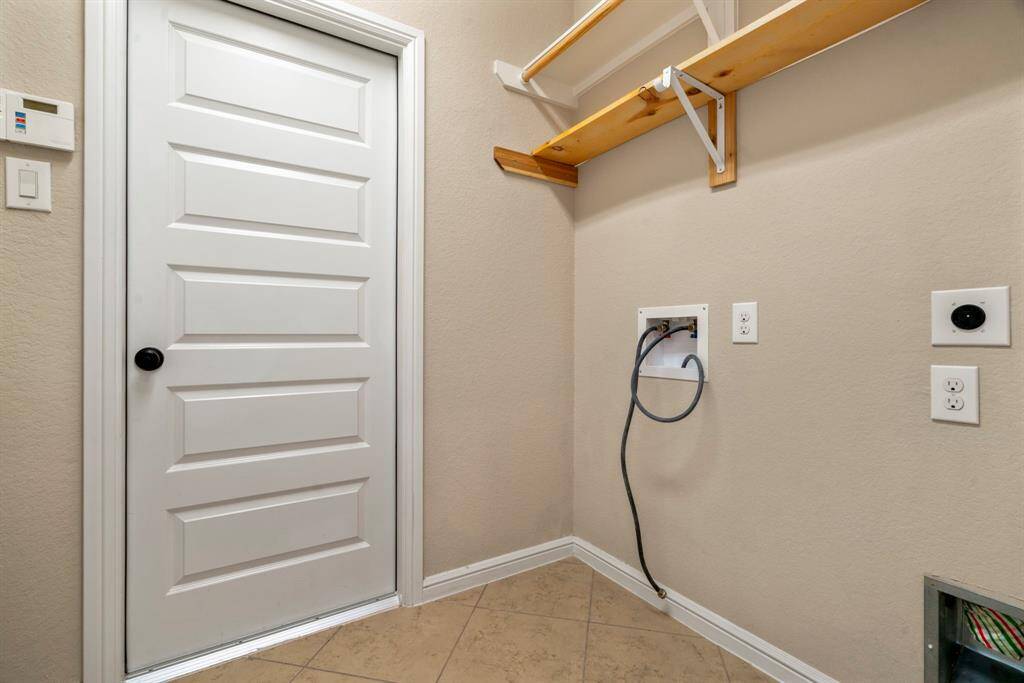 Efficient utility room with ample shelving and hookups for washer and dryer. Ideal for organizing laundry and storage needs.