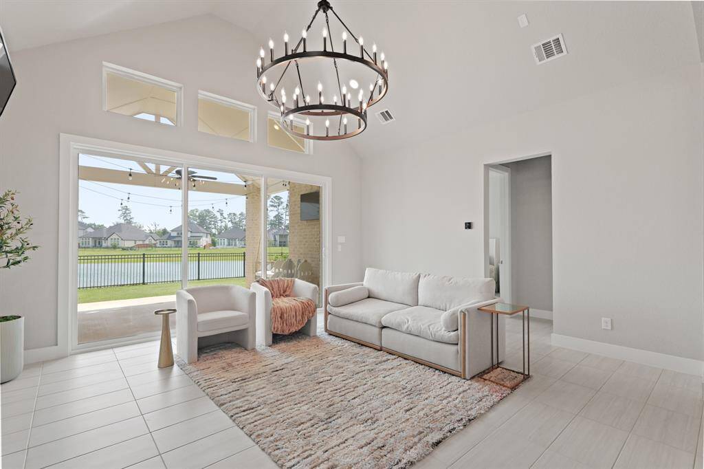 Floor-to-ceiling windows showcase breathtaking lake views and flood the living room with natural light, while a soaring ceiling and dramatic chandelier create a spacious, airy feel.