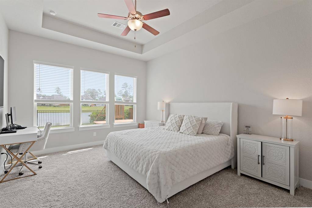 Wake up to peaceful lake views through three large windows in this spacious primary suite, complete with a tray ceiling and plush carpet for ultimate comfort.