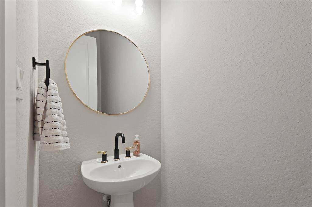 Sleek and modern half bath featuring a stylish pedestal sink, matte black faucet, and a gold-framed round mirror for a touch of elegance.
