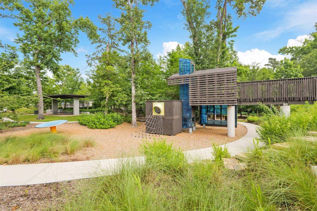 Uniquely designed playground with modern climbing structures, slides, and a treehouse-style bridge set among beautifully landscaped greenspace.