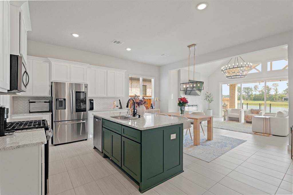 This open-concept kitchen shines with crisp white cabinetry, a striking green island, and stainless steel appliances—all flowing seamlessly into the dining and living areas with panoramic lake views through floor-to-ceiling windows.