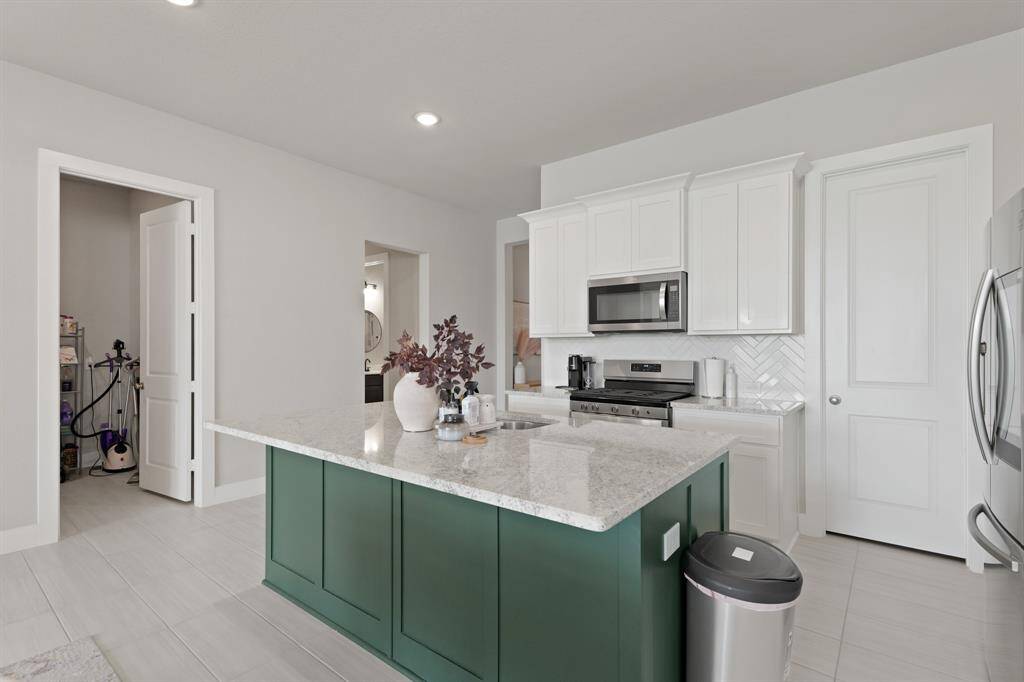 The chef’s kitchen features a built-in microwave, gas range, and stylish herringbone backsplash, while the large granite island provides ample prep and seating space.