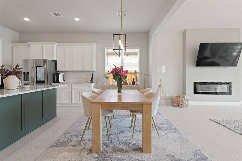 The dining area is enhanced by an upgraded pendant light and cozy views into the living room featuring a sleek wall-mounted electric fireplace.