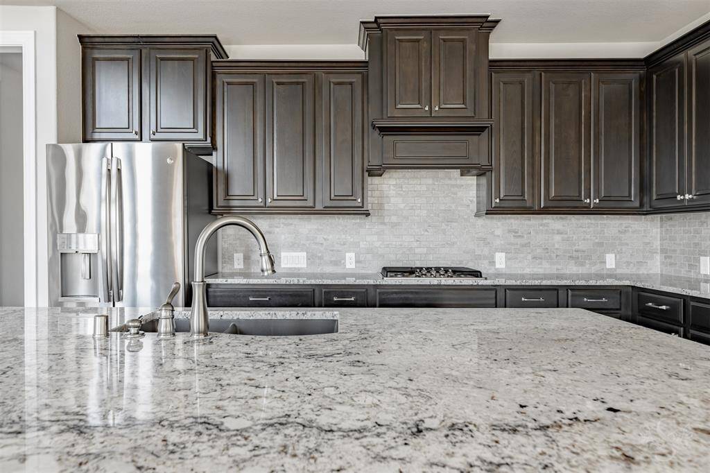 Close-up view of the gourmet kitchen highlights the stunning granite countertops and designer backsplash. The custom dark cabinetry adds depth and elegance to this refined culinary space.