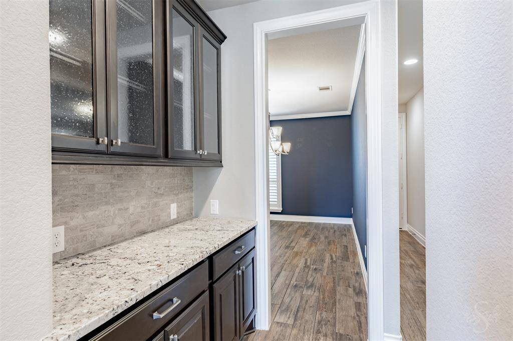 The butler’s pantry offers additional storage and serving space with beautiful granite counters and upper cabinets featuring decorative glass fronts. This convenient pass-through connects the kitchen and formal dining room with ease.