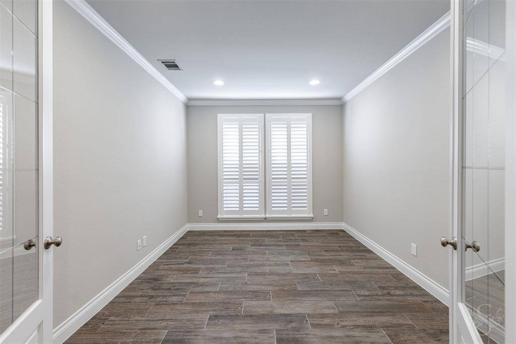 Double doors open to a sophisticated home office featuring plantation shutters, crown molding, and wood-look tile flooring. This light-filled space offers both elegance and privacy—perfect for working or studying from home in style.
